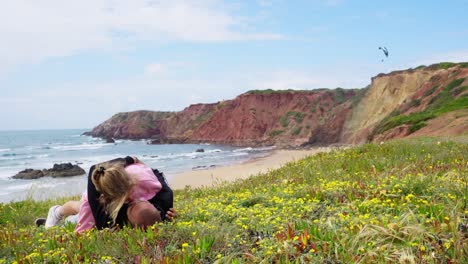 woman lies on top of her boyfriend lying on the flower field by the beach in algarve, portugal. - static shot
