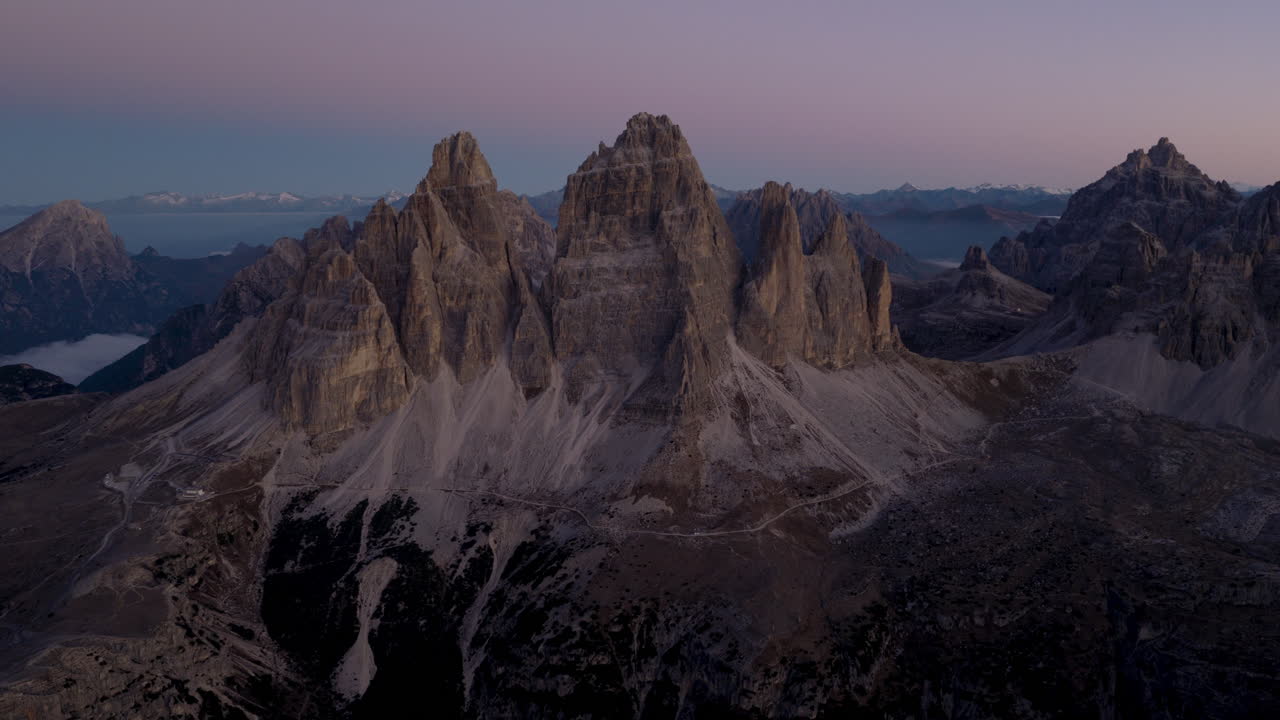 Cinematic aerial view of Dolomites Italy at sunrise, rugged rocky peaks above lush alpine hills and scattered chalets, serene mountain travel landscape nature scenery