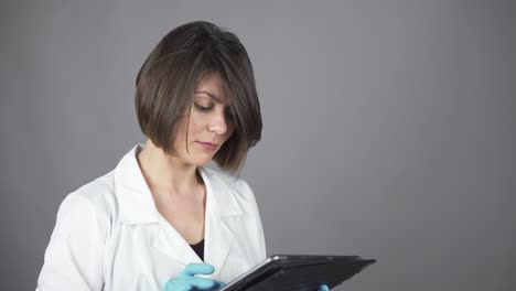 female doctor in blue rubber gloves using a tablet isolated on grey background. healthcare concept. shot in 4k.