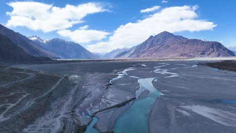 aerial drone shot showcasing a vehicle navigating the roads beside the flowing river in the vast nubra valley.