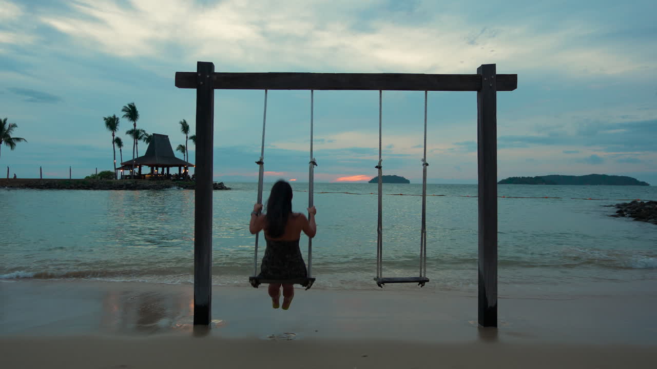 Rear View Of Woman Swinging On Beach Rope Swing Seafront At Colorful Sunset  - Shangri-la Tanjung Aru, Malaysia Free Stock Video Footage Download Clips