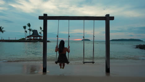 rear view of woman swinging on beach rope swing seafront at colorful sunset - shangri-la tanjung aru, malaysia
