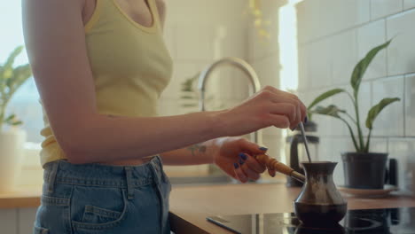 young woman preparing coffee in cezve on kitchen stove