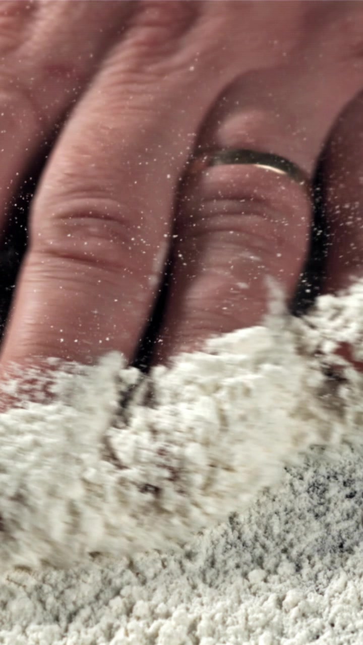 Primo piano di una mano che sparge farina bianca al rallentatore