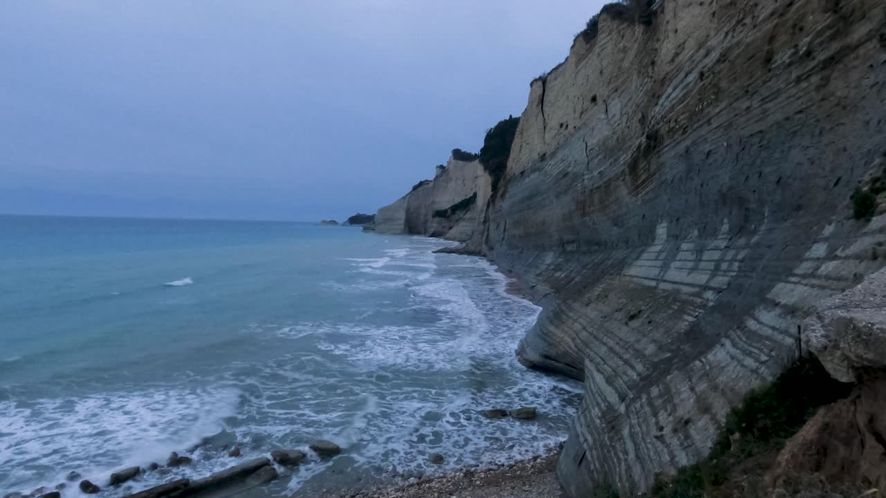 Dramatic coastline view featuring majestic clay cliffs and turquoise sea waves crashing on a pebbled beach during twilight, showcasing scenic Mediterranean nature and geological formations