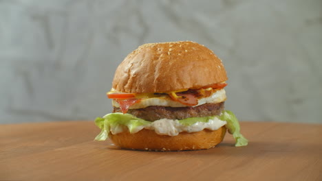 One-hamburger-on-a-board-fries-are-scattered-around.-Close-up-of-delicious-fresh-home-made-burger-with-lettuce-cheese-onion-and-tomato-on-a-rustic-wooden-plank-on-a-dark-background