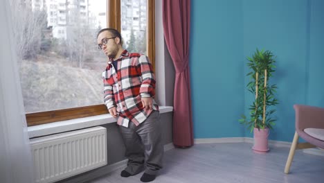 el hombre enano en su casa apoyando la cabeza en la ventana y mirando afuera.