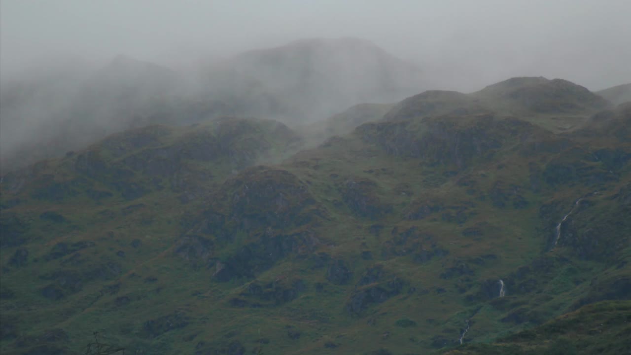 Timelapse of low hanging clouds passing through moody highland mountains