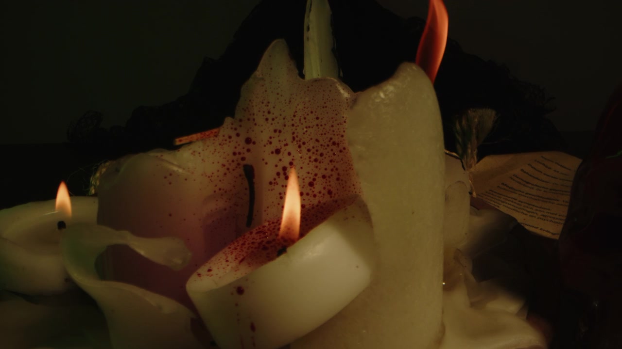 Carrellata inquietante in avanti di schizzi di sangue su candele accese su un altare occulto con un teschio di vetro