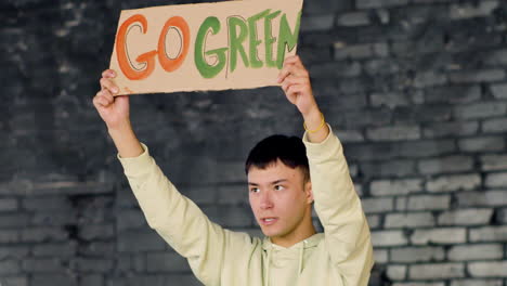 young asian environmental activist holding a cardboard with go green" inscription and protesting against climate change inaction"