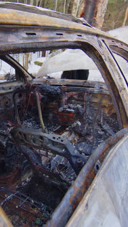 Crashed and burned out car wreck on snowy roadside, reckless driving. Vertical