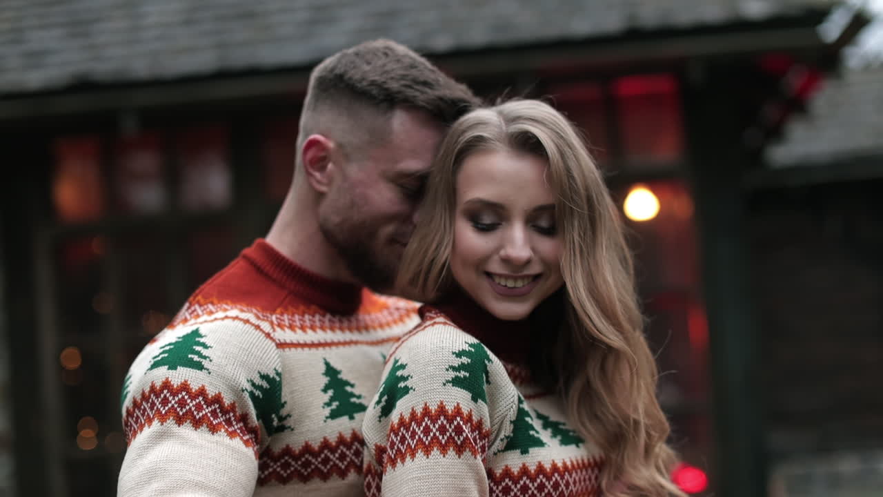 Affectionate couple stands hugging outside. Young pair in similar winter sweaters spending time together in the nature.