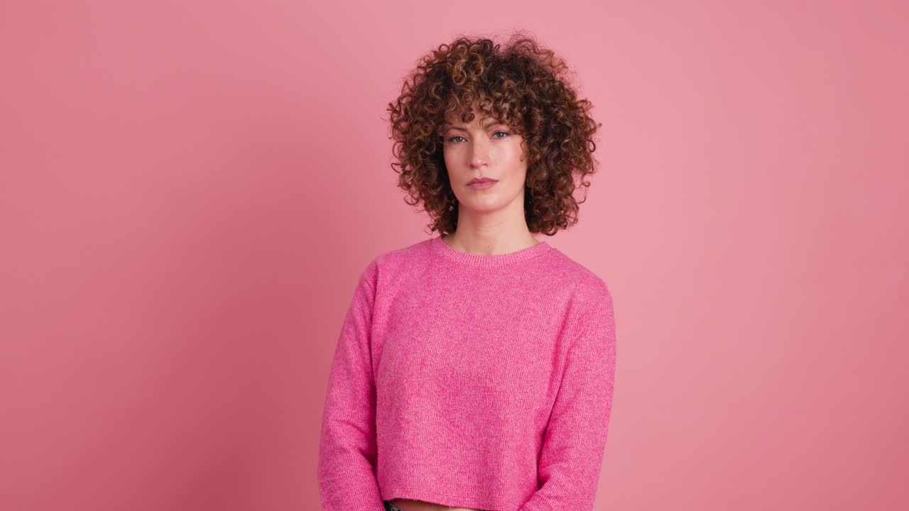 Stehende charmante junge Frau mit Locken vor rosa Hintergrund