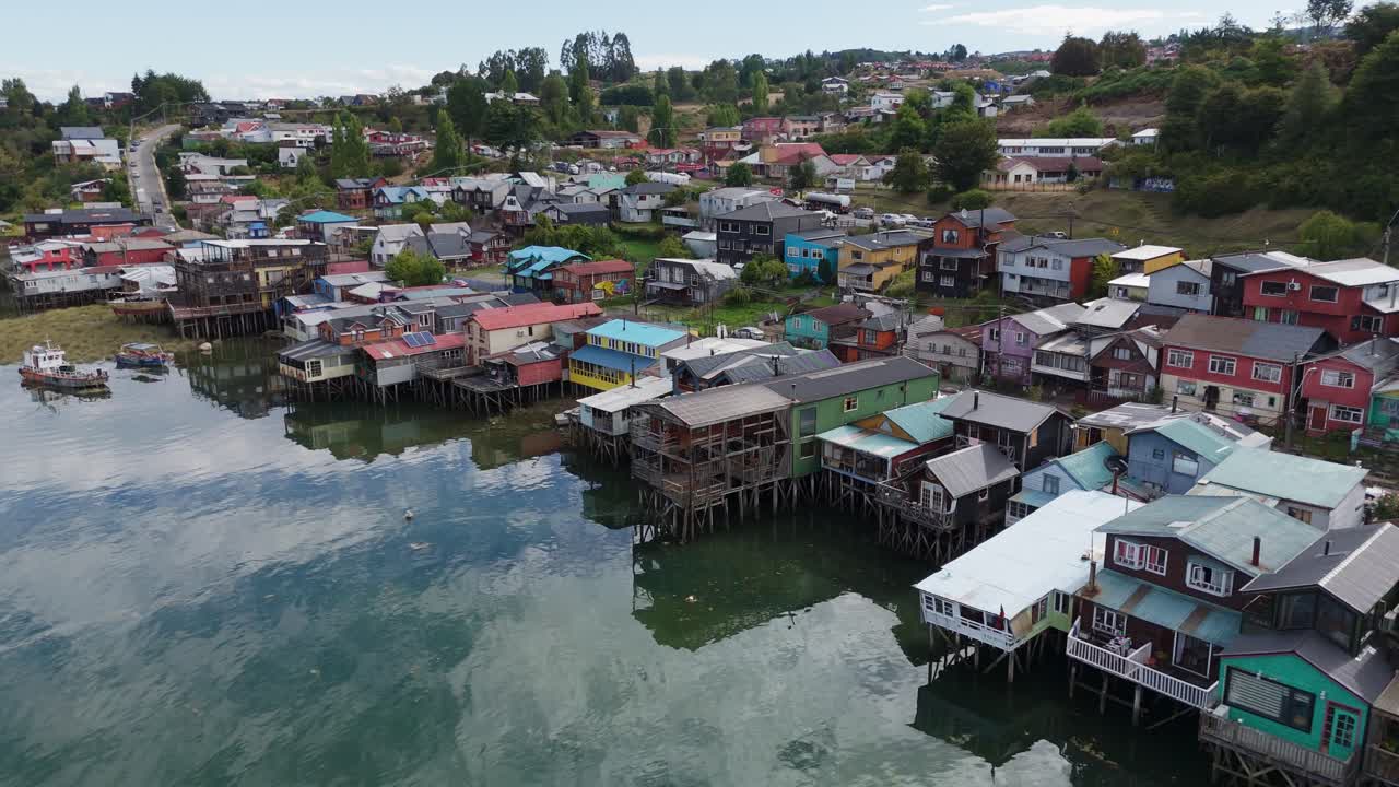 Aerial view of palafitos, traditional colorful wooden stilt houses, reflecting on the water in Castro, Chiloe Island, Chile. orbit motion shot