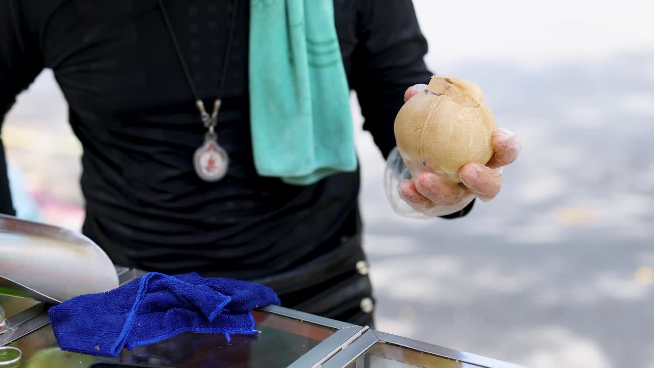 Vendor skillfully slices coconut with machete at outdoor market, natural daylight, steady close-up shot