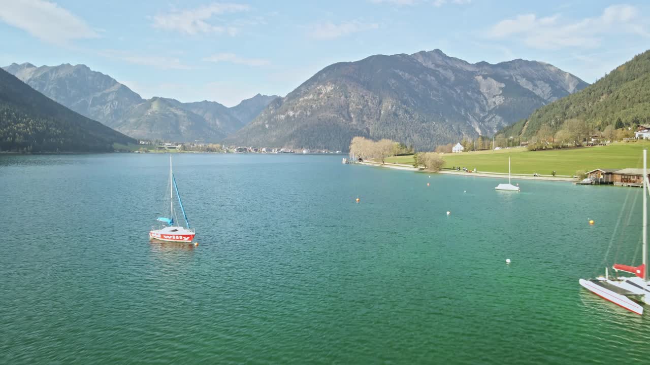 A beautiful drone shot at Achensee on a sunny summer day, flying by two boats gliding over vibrant turquoise water. The scene captures the tranquil beauty of Austria's largest alpine lake.