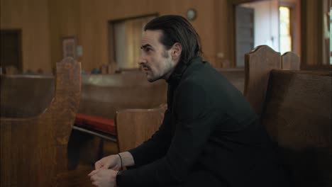 a sombre man in black suit sitting in pew in church in cinematic slow motion