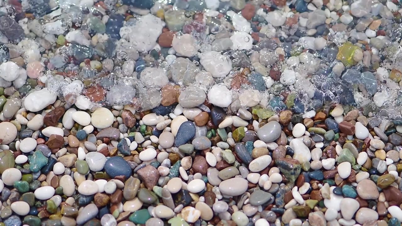 Acqua di mare limpida che si infrange su ciottoli colorati su una spiaggia