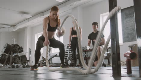 crossfit female bodybuilder working with battling ropes while gym buddies support her