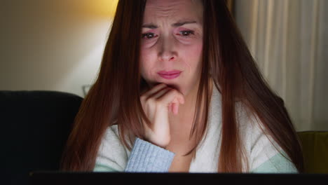 anxious woman sitting on sofa at home at night looking at laptop concerned about social media or bad news 2