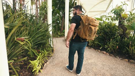 young male traveler with backpack walks through a tropical greenhouse in slow motion