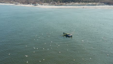 Antenne:-Möwenschwarm-Umringt-Fischer-In-Blauem-Boot,-Das-Netze-In-Der-Nähe-Der-Ostseeküste-Auswirft