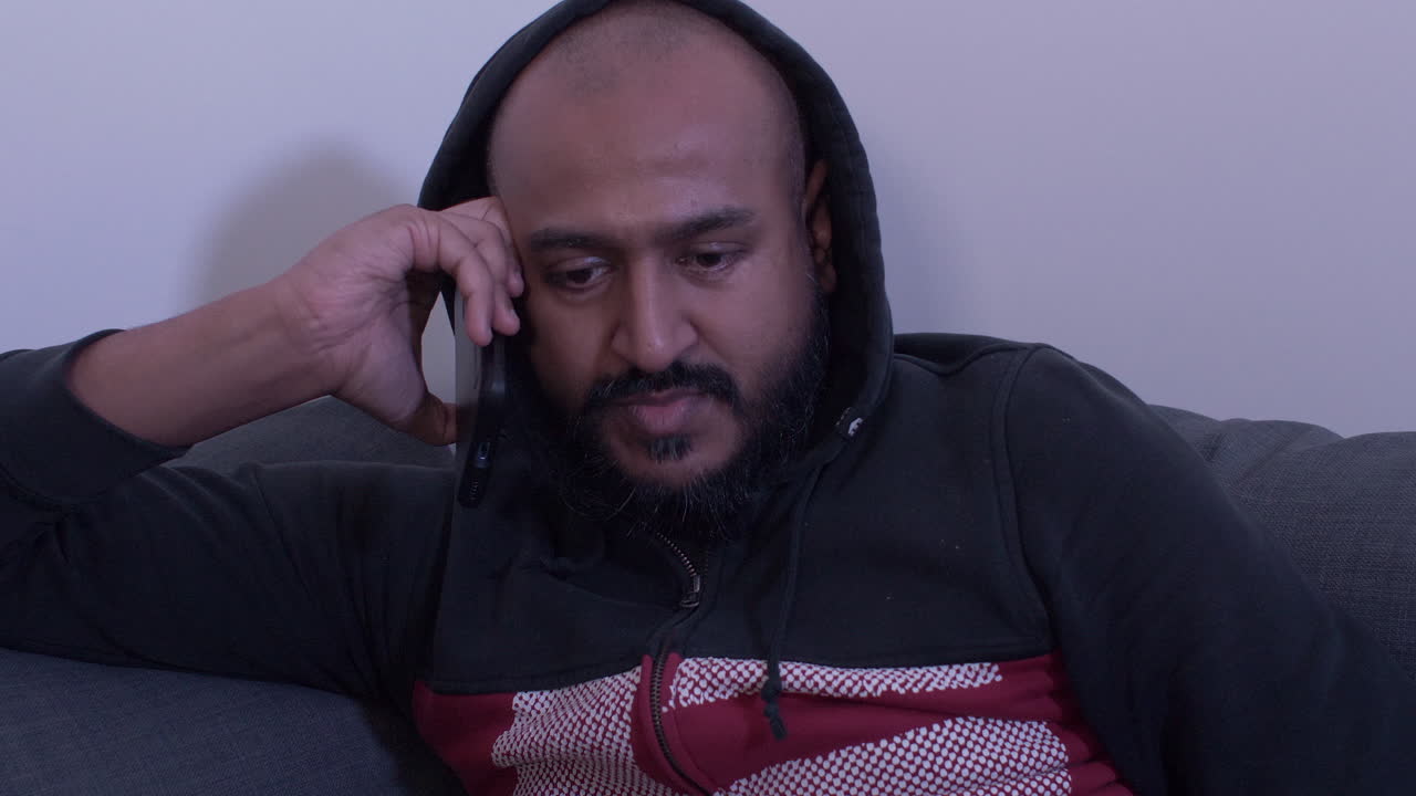 Hoodied Male Resting On Sofa Talking On Mobile Phone