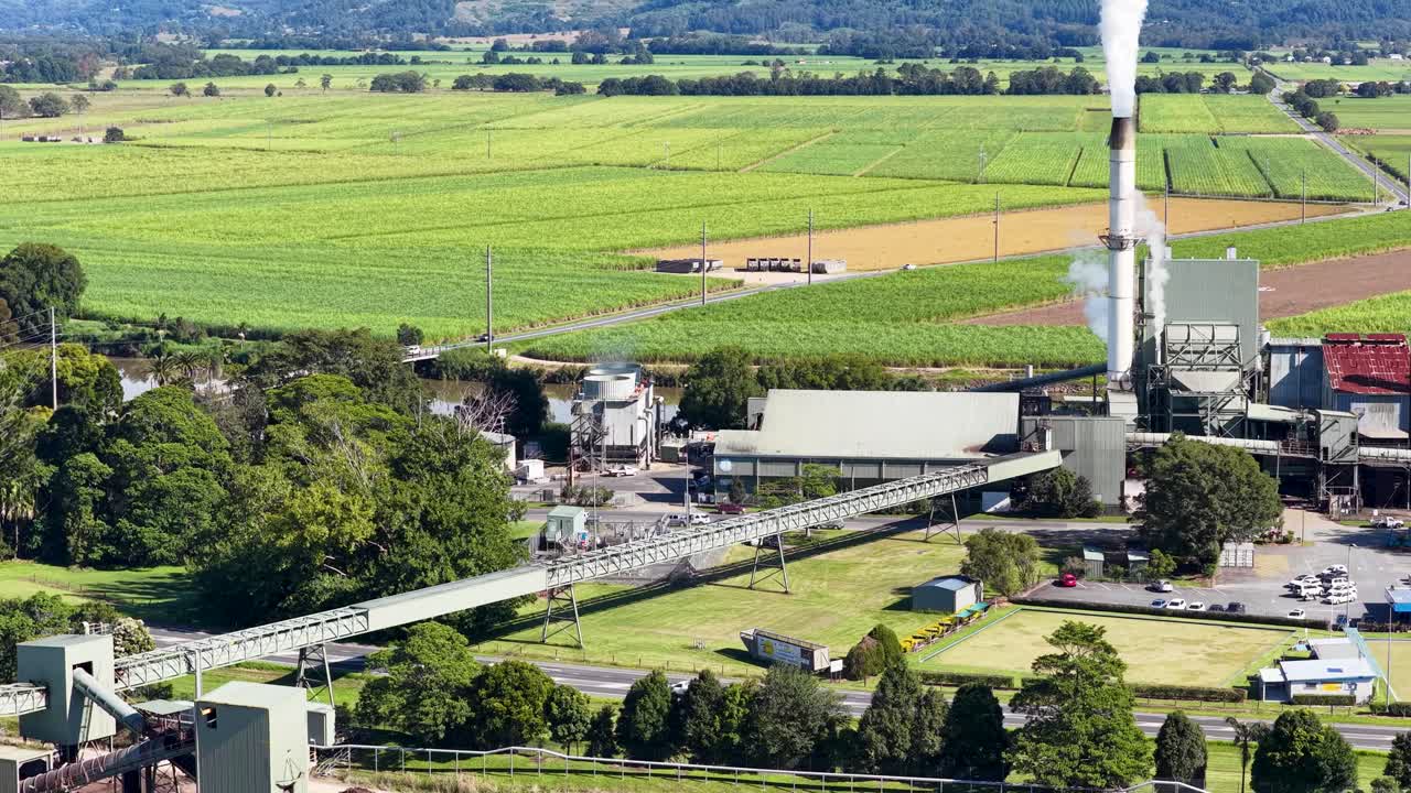 Aerial footage of a sugarcane factory surrounded by vast green fields under clear skies, highlighting industrial and agricultural landscapes