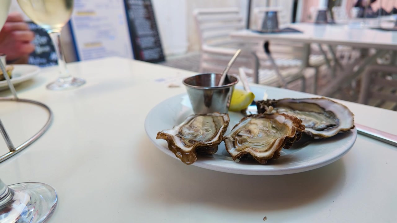 Close-up shot of fresh raw oysters on a white plate at an outdoor French restaurant