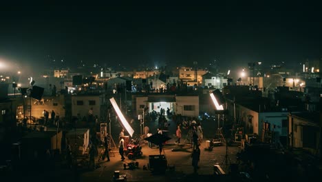 a nighttime cinematic production unfolds over rooftops, showcasing a dynamic film set surrounded by urban structures and illuminated by bright lights