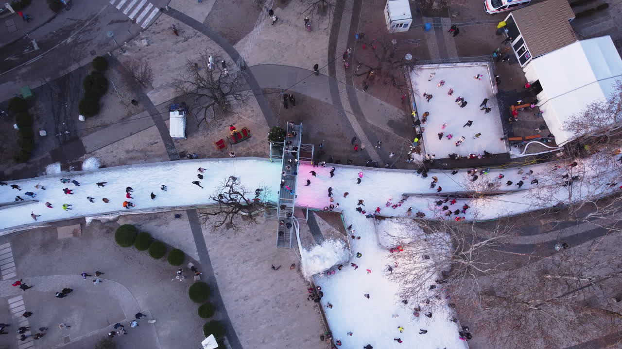 Drone clip of skaters navigating snowy tracks beside residential buildings in winter town