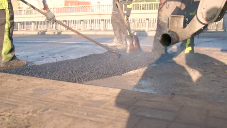 machine distributes hot asphalt onto road while a team of workers spread it out