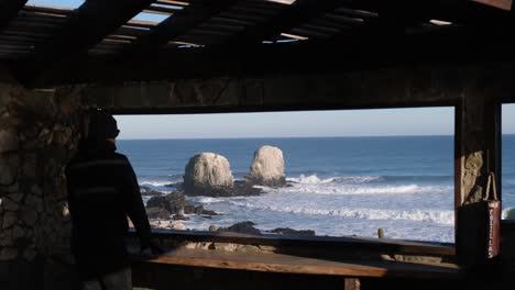 man looks through a frame or a window towards punta de lobos surf point chile without a face mask in the new normal of chile pichilemu