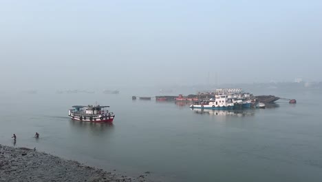 fotografía cinematográfica de un ferry navegando por un río y algunas personas bañándose en una mañana de invierno en el ghat del río hooghly en calcuta, india