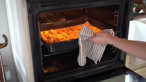 Mujer-Poniendo-Una-Bandeja-Para-Hornear-De-Pollo-Cubierto-Con-Copos-De-Maíz-En-El-Horno