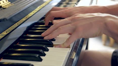 un primer plano de un hombre tocando un piano negro con las manos a la luz de una ventana