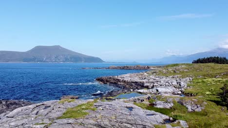 Aerial-view-of-the-rugged-coastline-in-Møre-og-Romsdal,-Norway,-featuring-clear-blue-waters,-rocky-shores,-and-distant-mountains