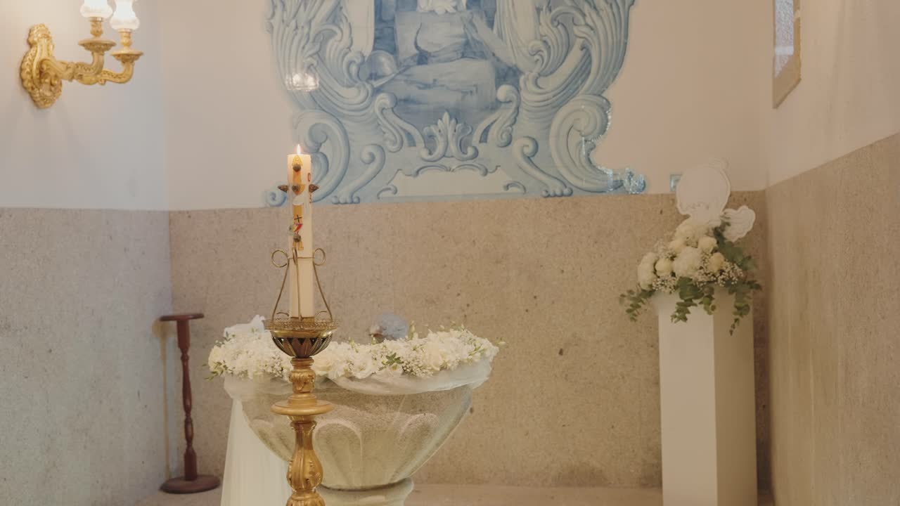 Pila bautismal discreta con vela y decoración floral dentro de la iglesia