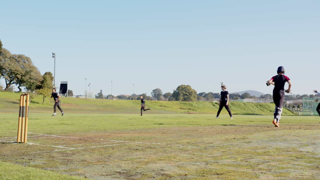 Cricket players running between wickets on sunny day at sports field