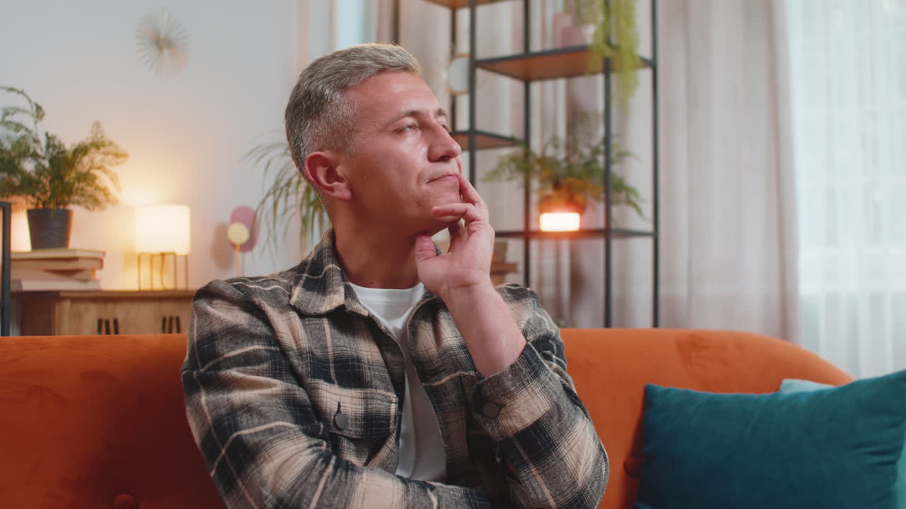 Thoughtful man sitting at home looks pensive thinks of unrequited love depressed bad feeling burnout