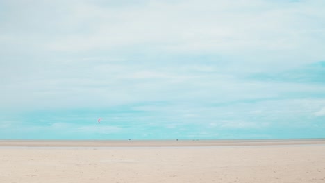 Ein-Kitesurfer-Schnitzt-In-Der-Ferne-Im-Wasser-Des-Ozeans-Bei-Ebbe,-Während-Schöne-Weiße-Wolken-Darüber-Schweben-Und-Vielleicht-Einen-Sturm-Zusammenbrauen