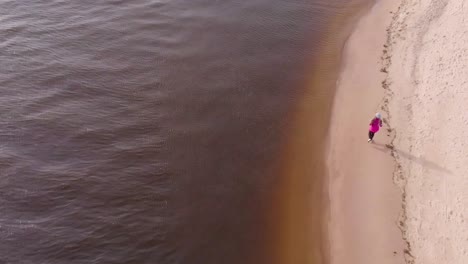 Female-jogger-runs-on-the-seashore-on-white-sand-beach-in-Europe,-aerial-establishing-view