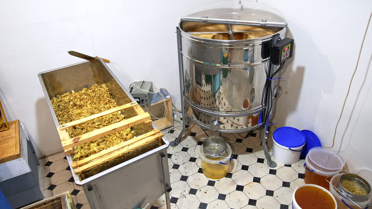 Little room in the apiary for harvesting honey. Electric machine extractor working in the corner. Few buckets are filled with freshly removed honey.