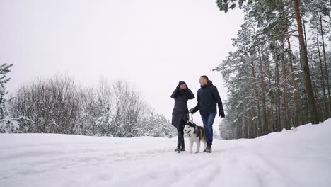 waist up portrait of happy modern couple playing with cute husky puppy outdoors in winter, focus on asian man smiling at camera