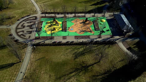 Drone-shot-of-a-playground-with-children-and-people-playing,-surrounded-by-trees-and-nature