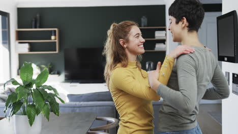 una feliz pareja de lesbianas caucásicas abrazándose y bailando en una cocina soleada