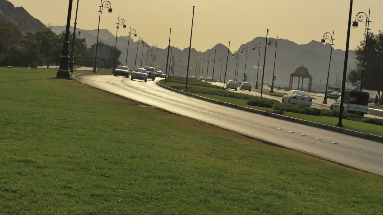 Curved road lined with ornate lamps and mountains in the background during golden hour