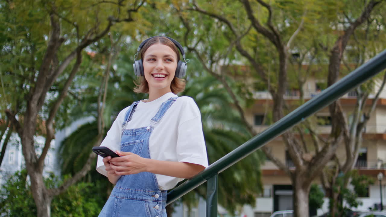 Headphones woman listening music holding mobile phone on green street closeup
