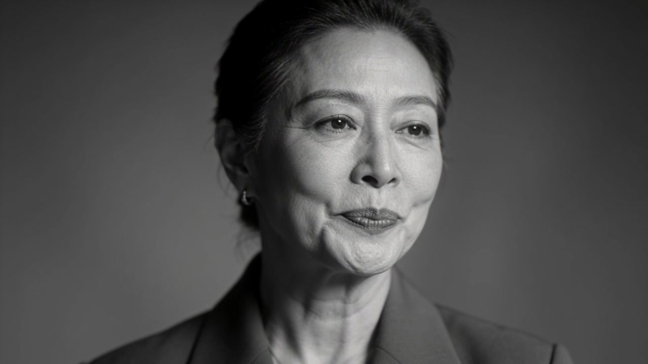 Answering prompt, senior Asian woman speaking, turning head right in studio, wearing blazer, studs