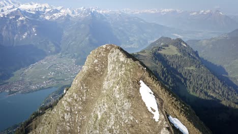 man hiking on beautiful ridge top amongst huge mountains and above a green valley with a blue lake